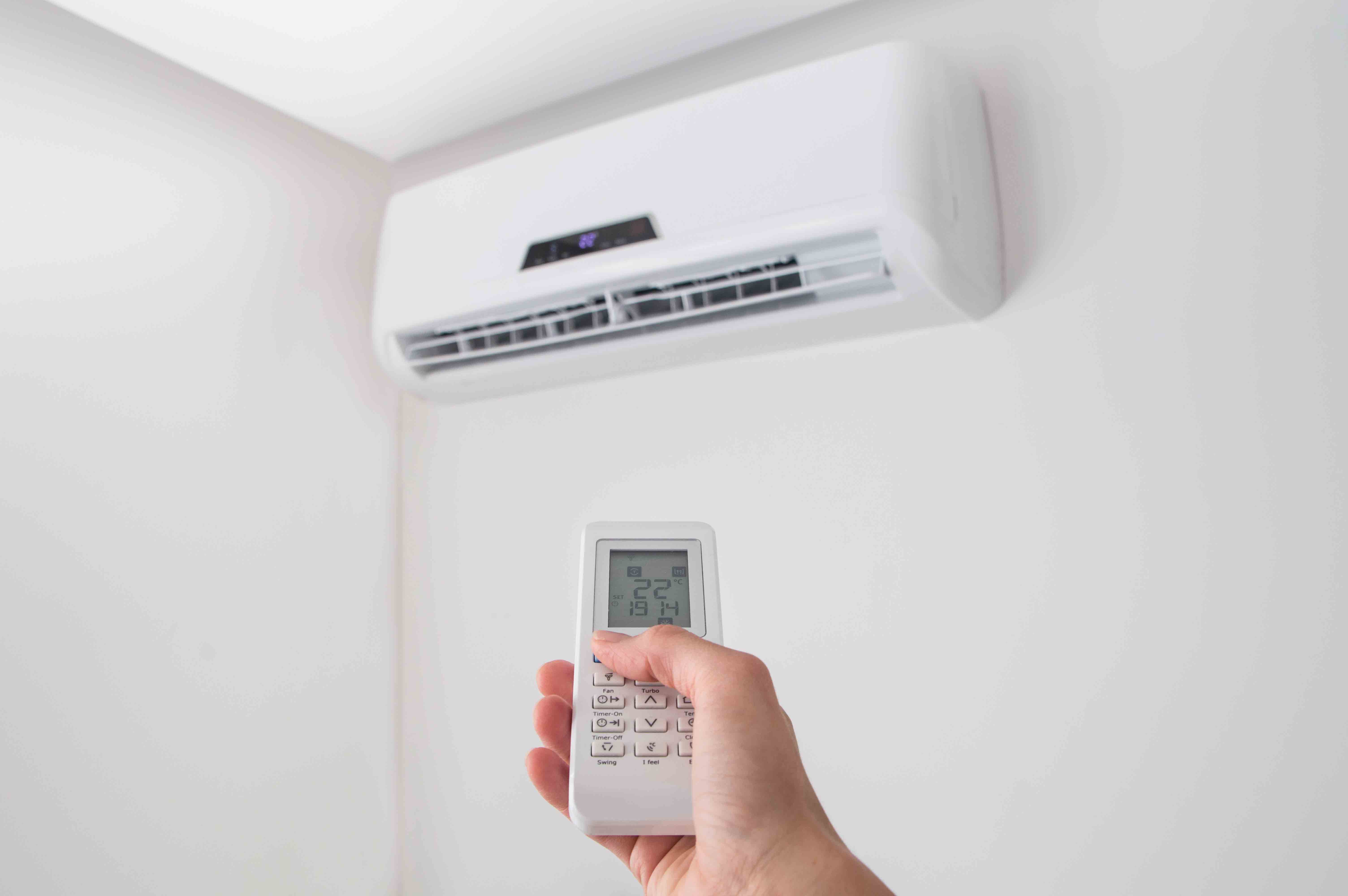 Hand,Holding,Remote,Control,,Adjusting,Temperature,Of,Air,Conditioner,Mounted